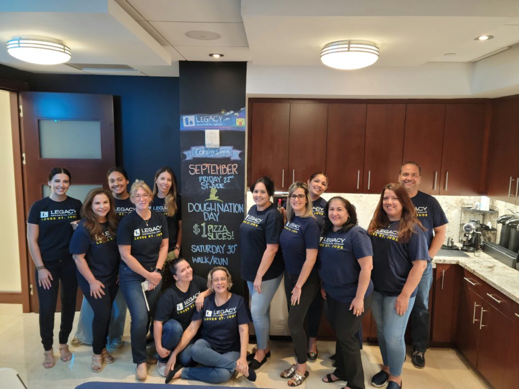 A group of Legacy Residential Group employees posing indoors around a chalkboard sign promoting the 2023 St. Jude Walk/Run event and other upcoming activities.